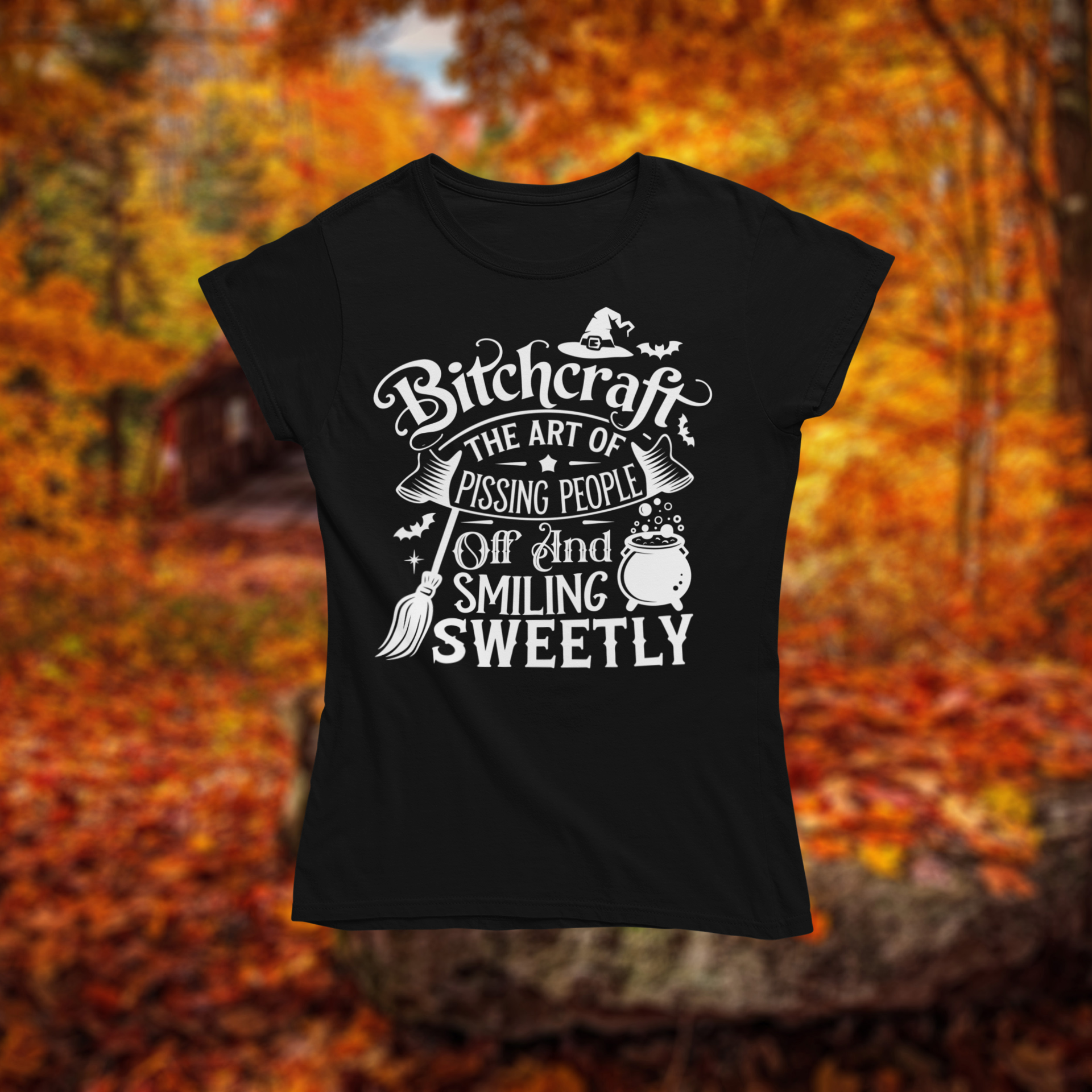 Black t-shirt with white text design "Bitchcraft" on a background of autumn leaves