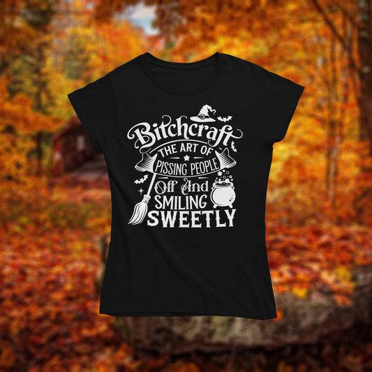 Black t-shirt with white text design "Bitchcraft" on a background of autumn leaves